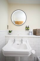 A bathroom with a white sink, a round mirror, a potted plant, and toiletries on the countertop.