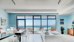 A spacious living area with a large sliding glass door leading to a balcony with a view of the ocean. - Surferscorner (Cape Town)