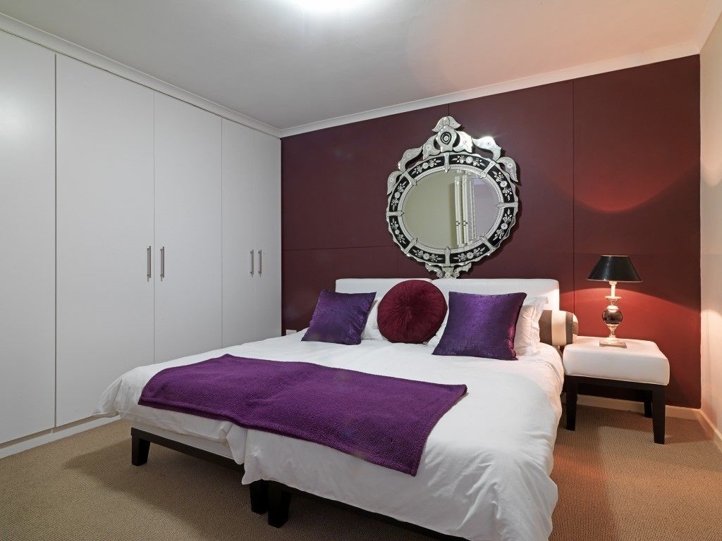 A bedroom with a bed, a large mirror, a nightstand, and a wardrobe.