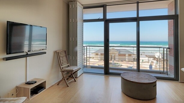 A modern living room with a large window offering a view of the beach. - Surferscorner (Cape Town)