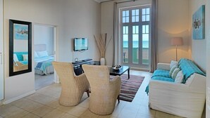 A living room with a sofa, two wicker chairs, a coffee table, a TV, and a large window with curtains. - Surferscorner (Cape Town)