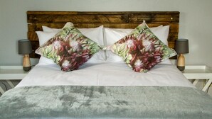A bed with a wooden headboard, two floral pillows, a grey blanket, and two bedside lamps.
