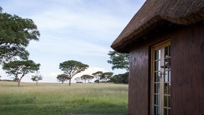 Une construction en bois avec un toit de chaume, une terrasse en bois et une porte dotée de panneaux de verre.