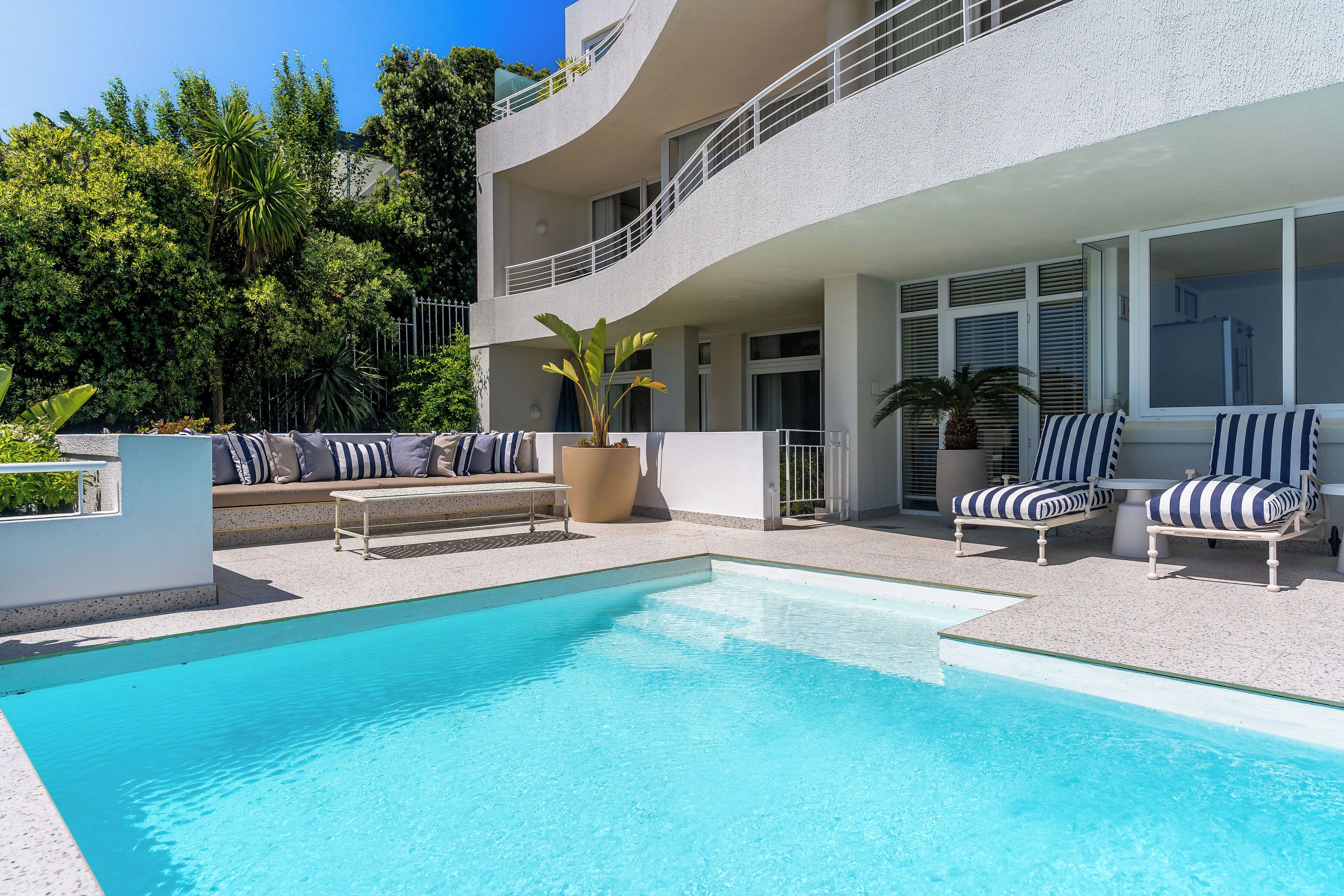 Un espace piscine moderne avec une piscine à l’eau d’un bleu limpide, des chaises longues et un coin salon agrémenté de coussins.