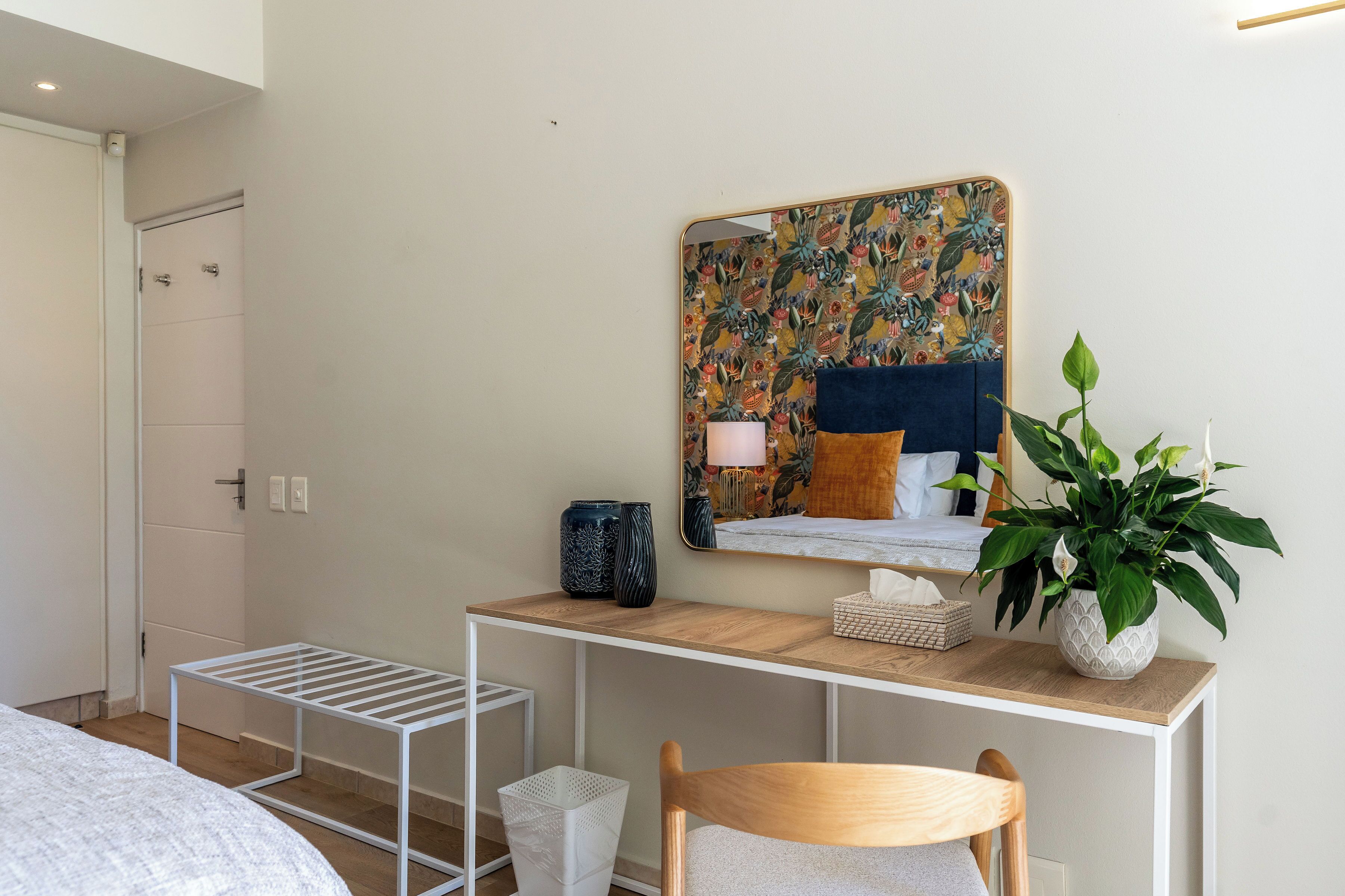 A bedroom with a bed, a desk with a mirror, a potted plant, and a bedside table.