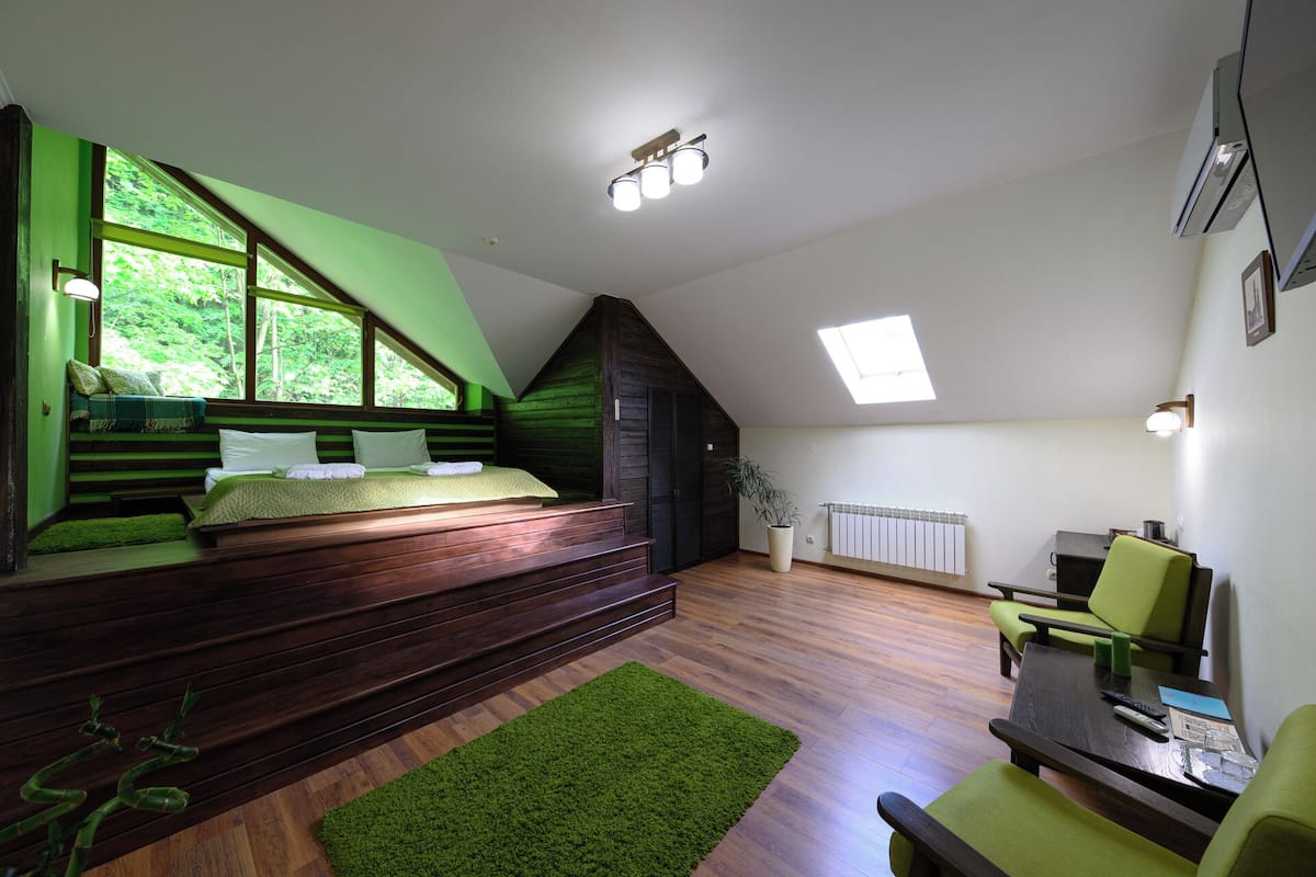 Un dormitorio con una cama alta, un sofá verde, una mesita y un radiador.