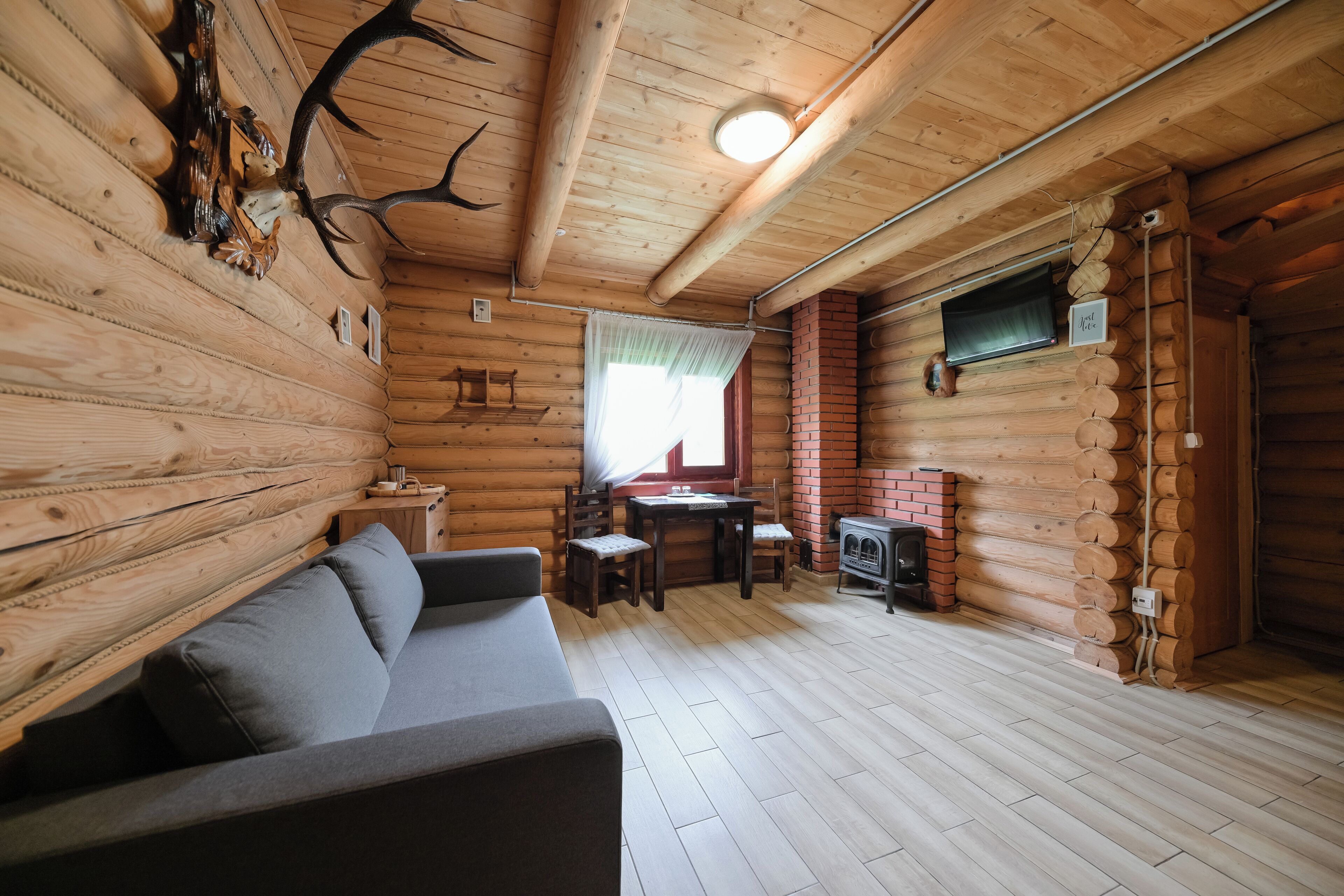 En stuga byggd av timmer med en soffa, ett matbord, stolar och en öppen spis.