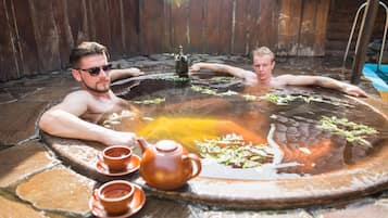 Relax in a serene hot spring bath surrounded by a fence, with a tea service at hand.