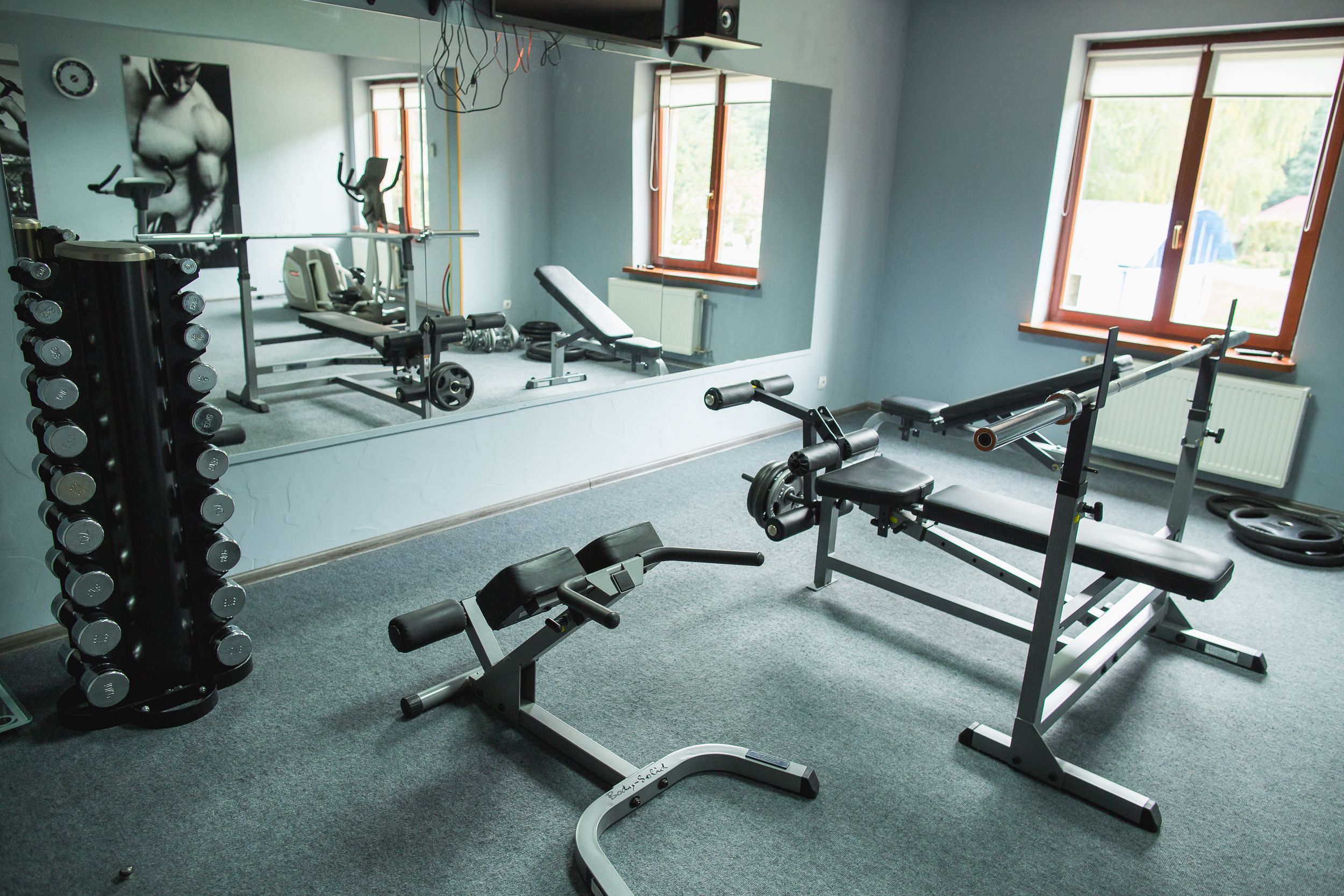 A gym with exercise equipment, a mirror, and windows.