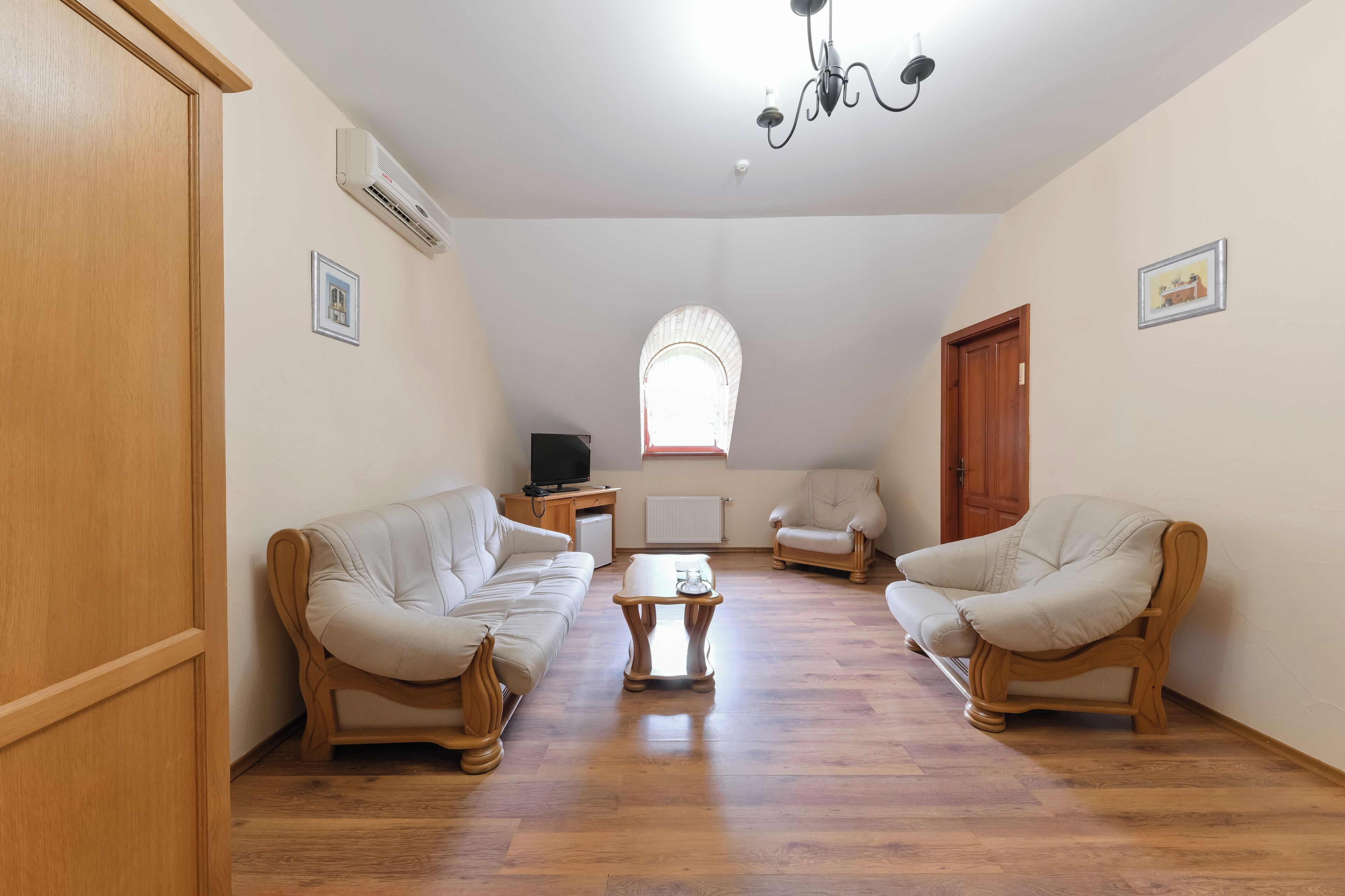 Ein geräumiges Wohnzimmer mit zwei weißen Ledersofas, einem Holztisch und einer Chandelüster.