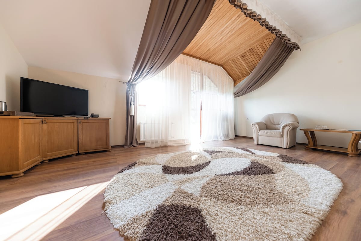 Una sala de estar con una televisión de pantalla plana, armarios de madera, un sillón beige, una mesita y una alfombra estampada.