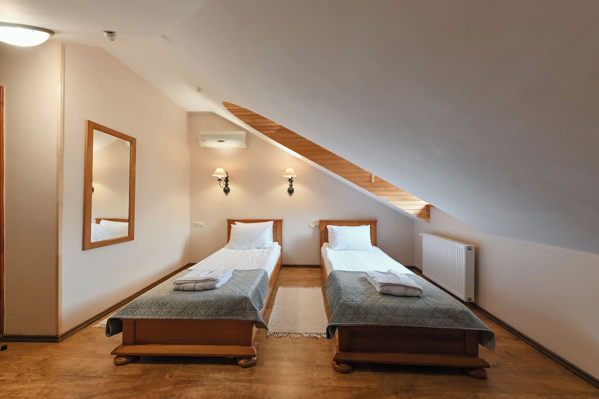 Una habitación con dos camas individuales, techo de madera, un espejo, apliques en la pared y un radiador.