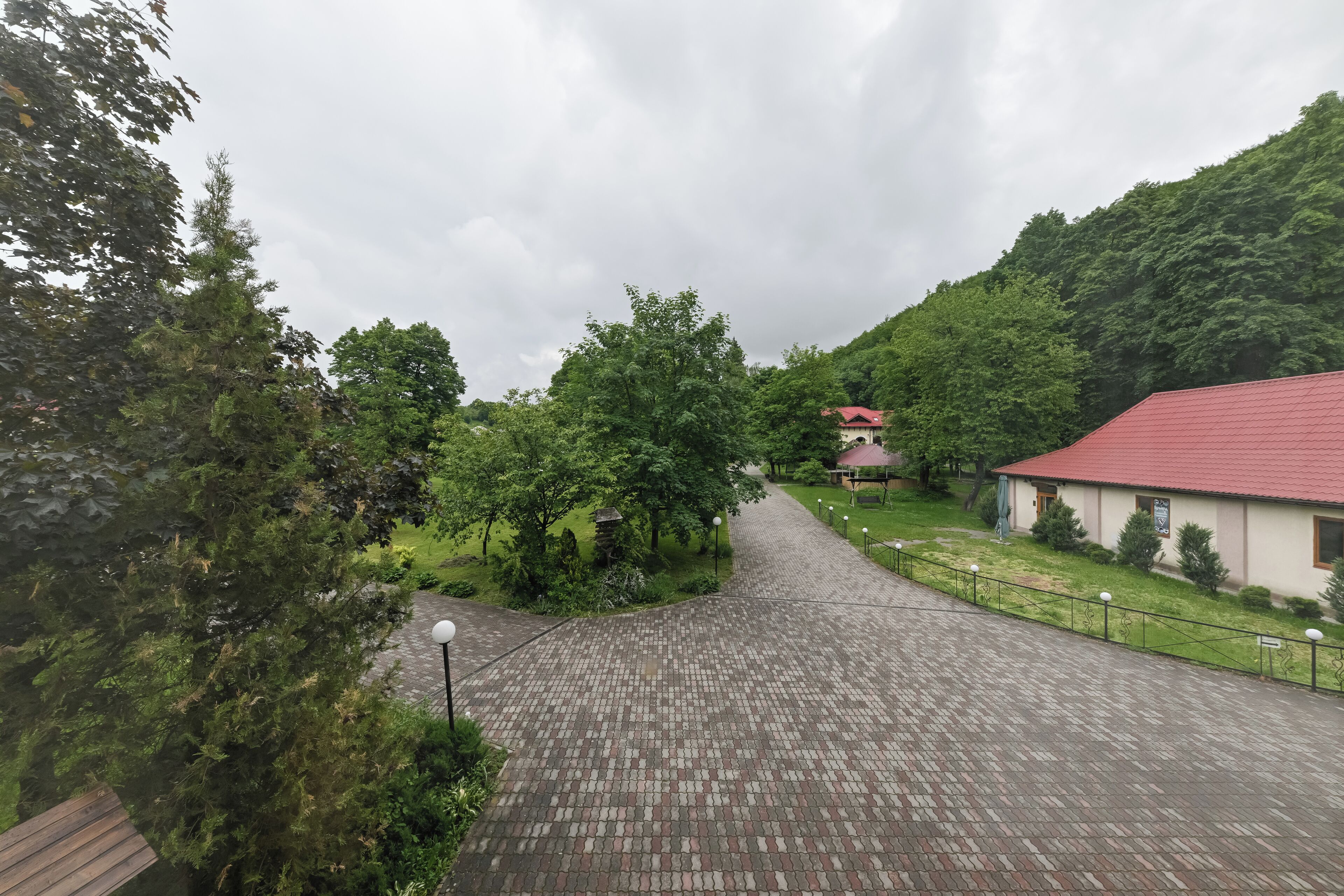 A paved pathway leading to a building with a red roof, surrounded by lush greenery and trees.