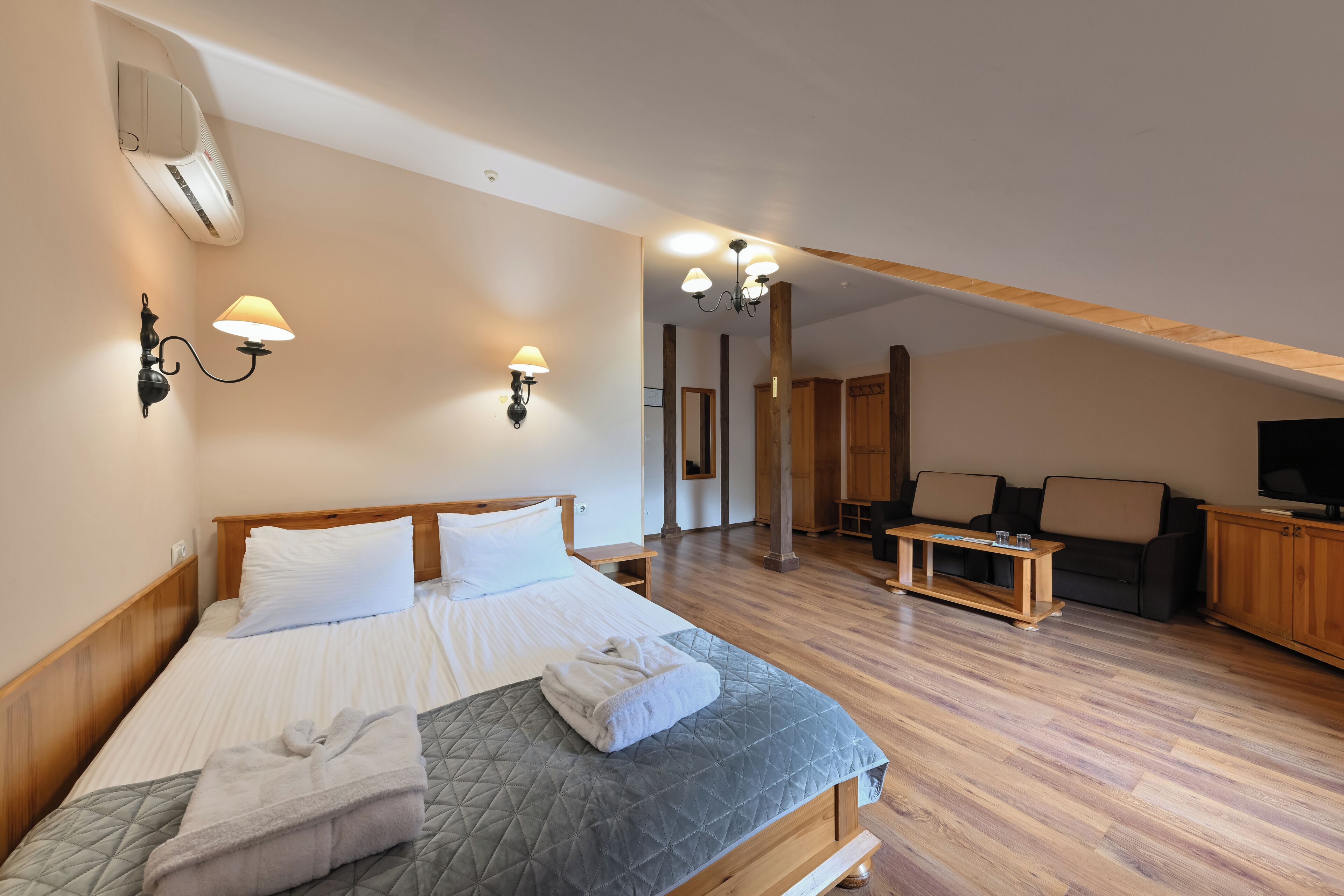 Una habitación de hotel con cama, lámparas de noche, un banco de madera, televisión y mueble para televisor.