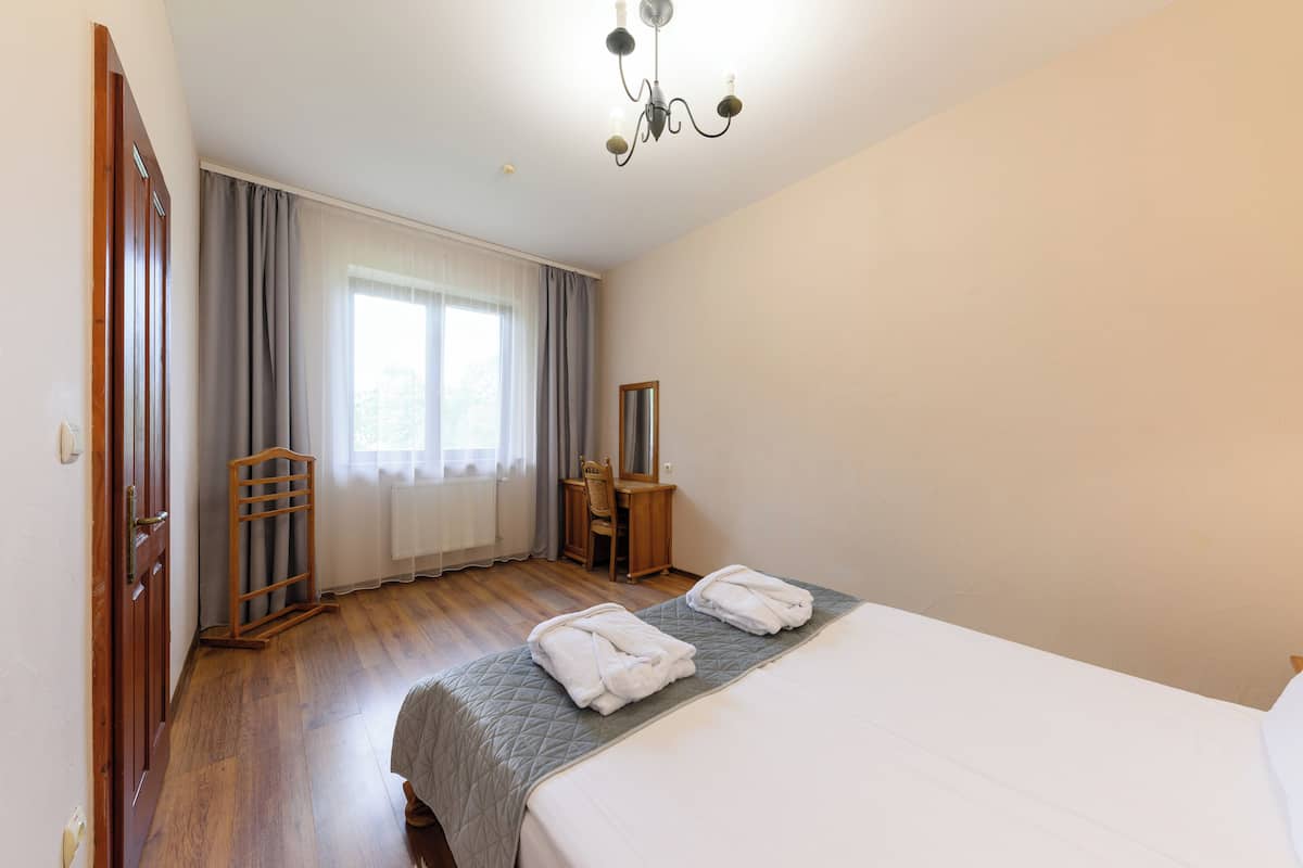 Una habitación de hotel con una cama, un aparador de madera, una silla y una ventana con cortinas.