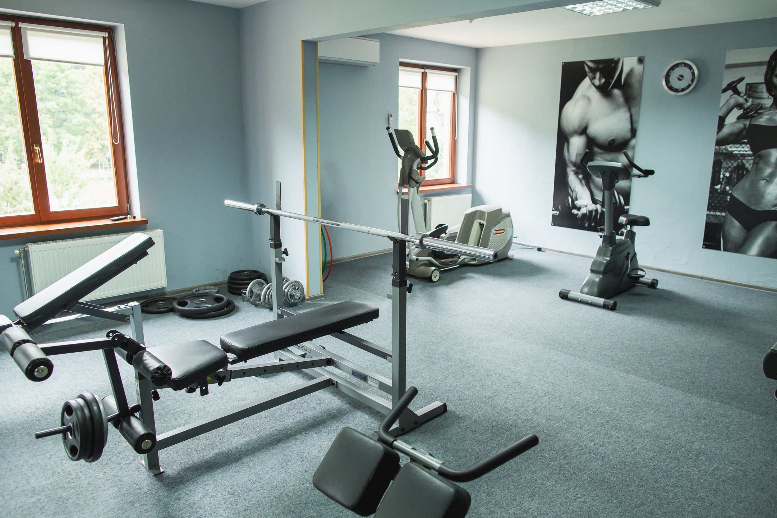 Un gimnasio con equipo de ejercicio, una banca y una pared con carteles de fitness.
