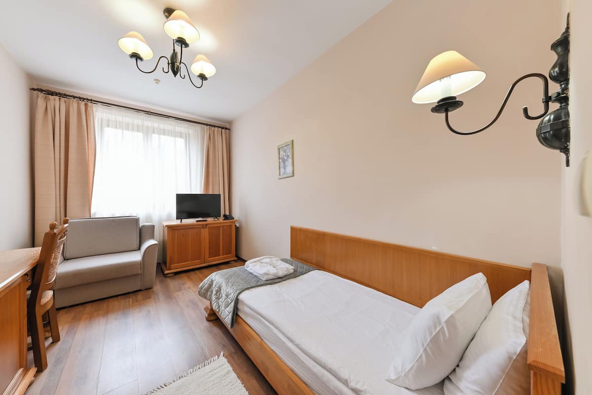 Una habitación de hotel con cama, sofá, televisión, armario de madera y candelabro.