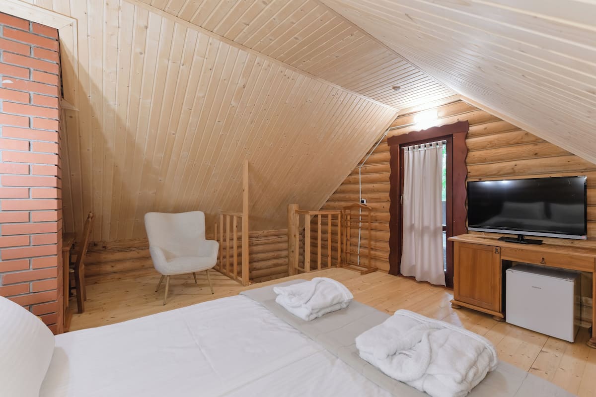 Una habitación tipo cabaña de madera con una cama, una silla blanca, un televisor y un refrigerador pequeño.