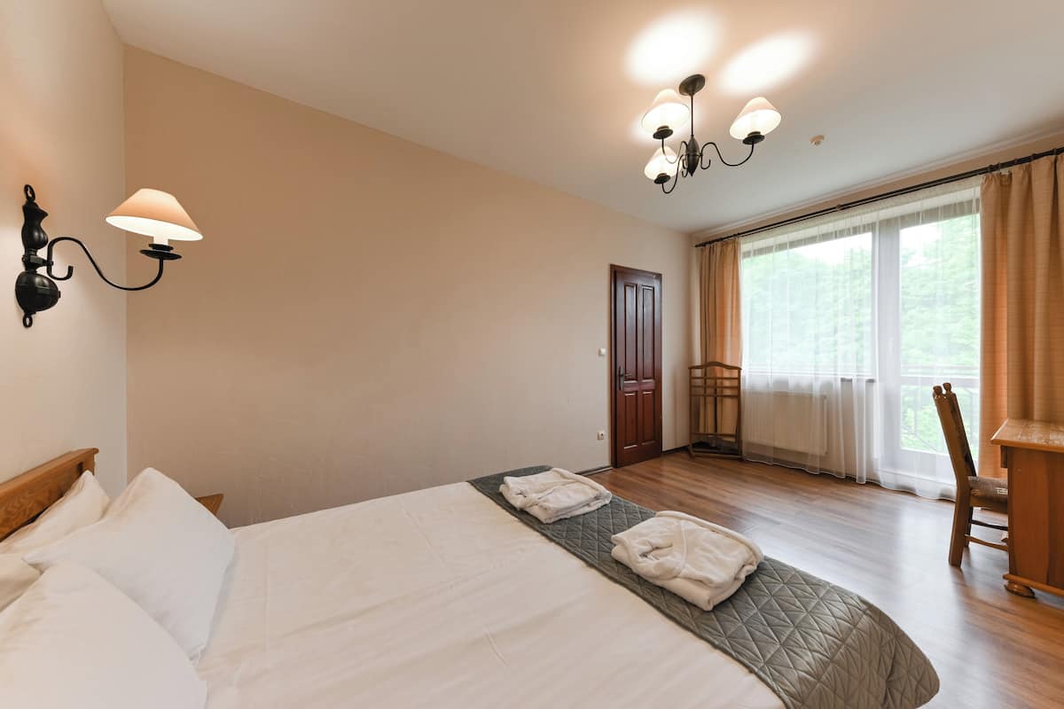 Habitación de hotel con cama, escritorio, silla y un ventanal con cortinas.