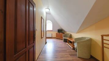 A narrow hallway with wooden flooring leading to a room with a sloped ceiling and a window.