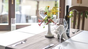 Une table à manger dressée avec un vase de fleurs, des verres à vin et des couverts.