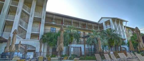 A hotel with outdoor seating, palm trees, and a multi-story building with balconies.