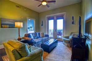 A living room with a sofa, ottoman, and armchair, a ceiling fan, and a large window with blinds.