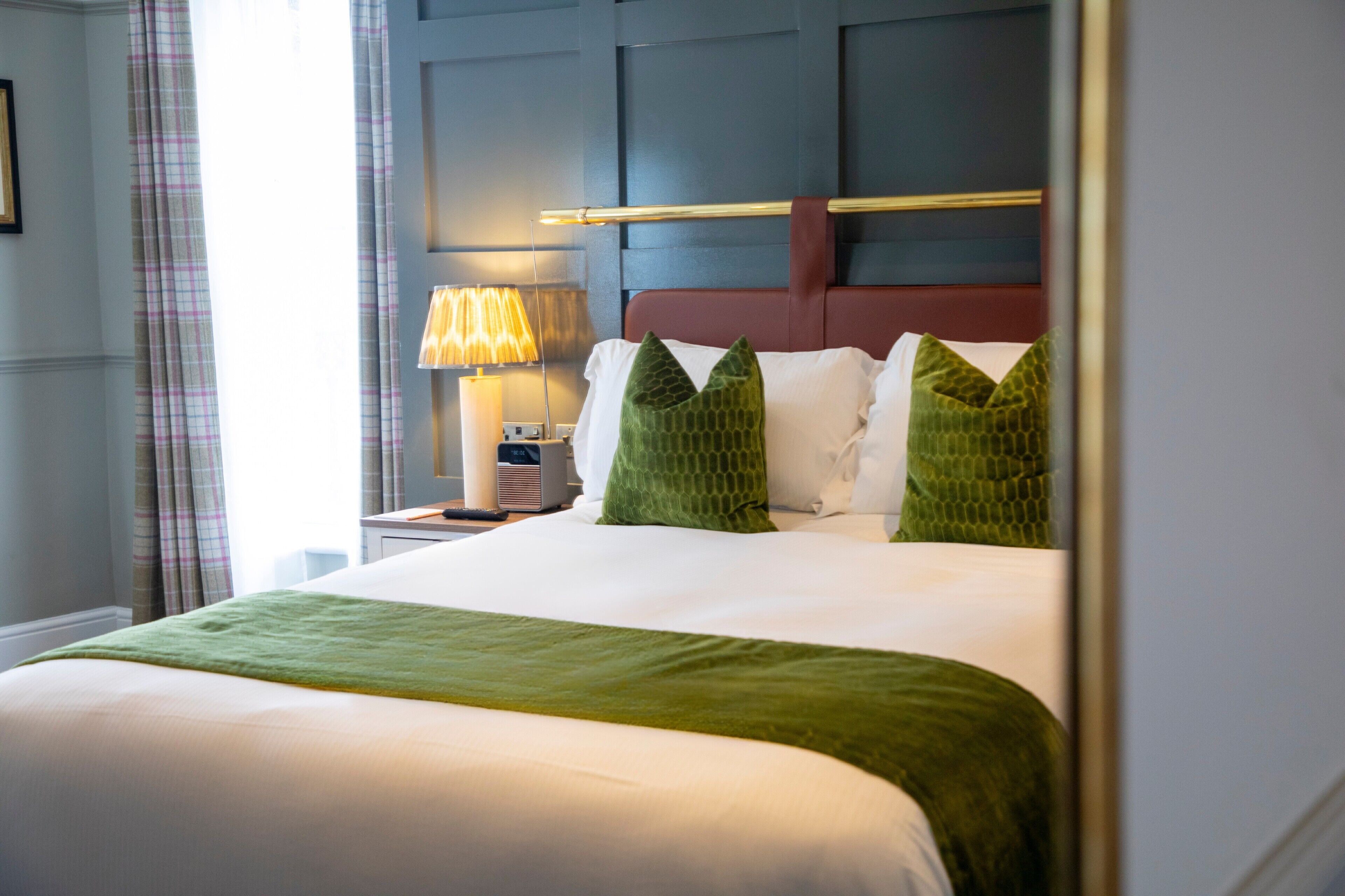 A neatly made bed with a green throw, a bedside lamp, and a headboard with a horizontal bar.