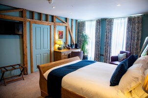 A bedroom with a wooden bed, a desk with a lamp, a chair, a television on the wall, and curtains on the windows.