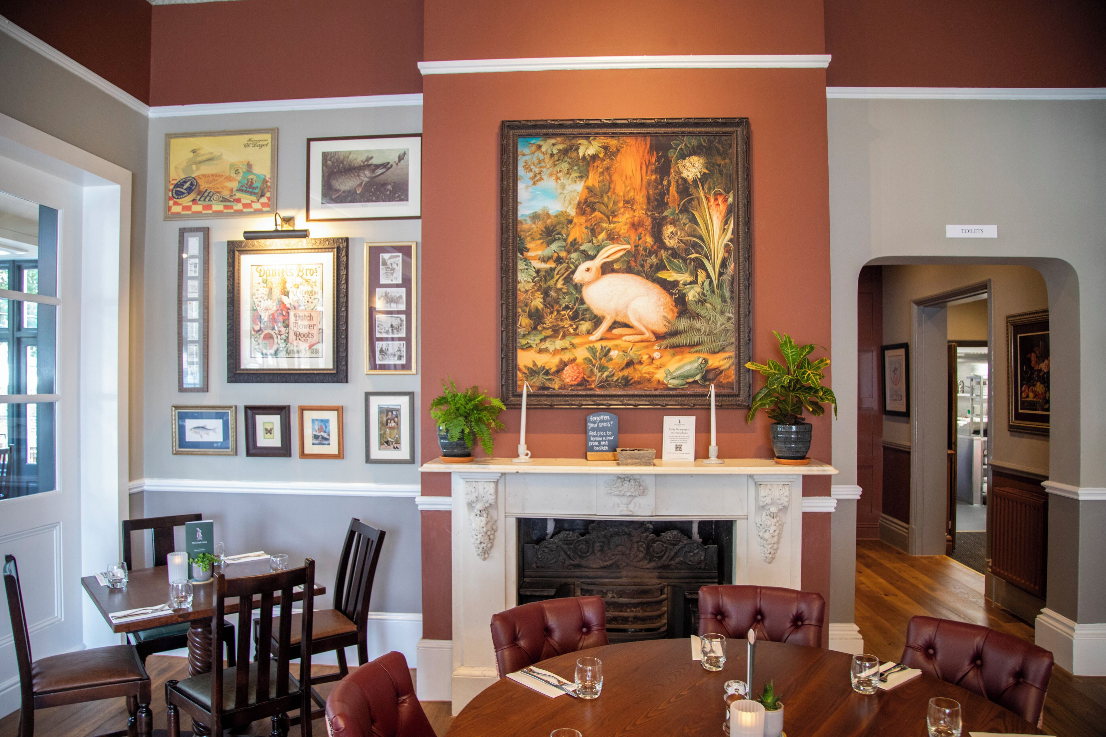 A dining room with a fireplace, framed artwork, and a table set for four.