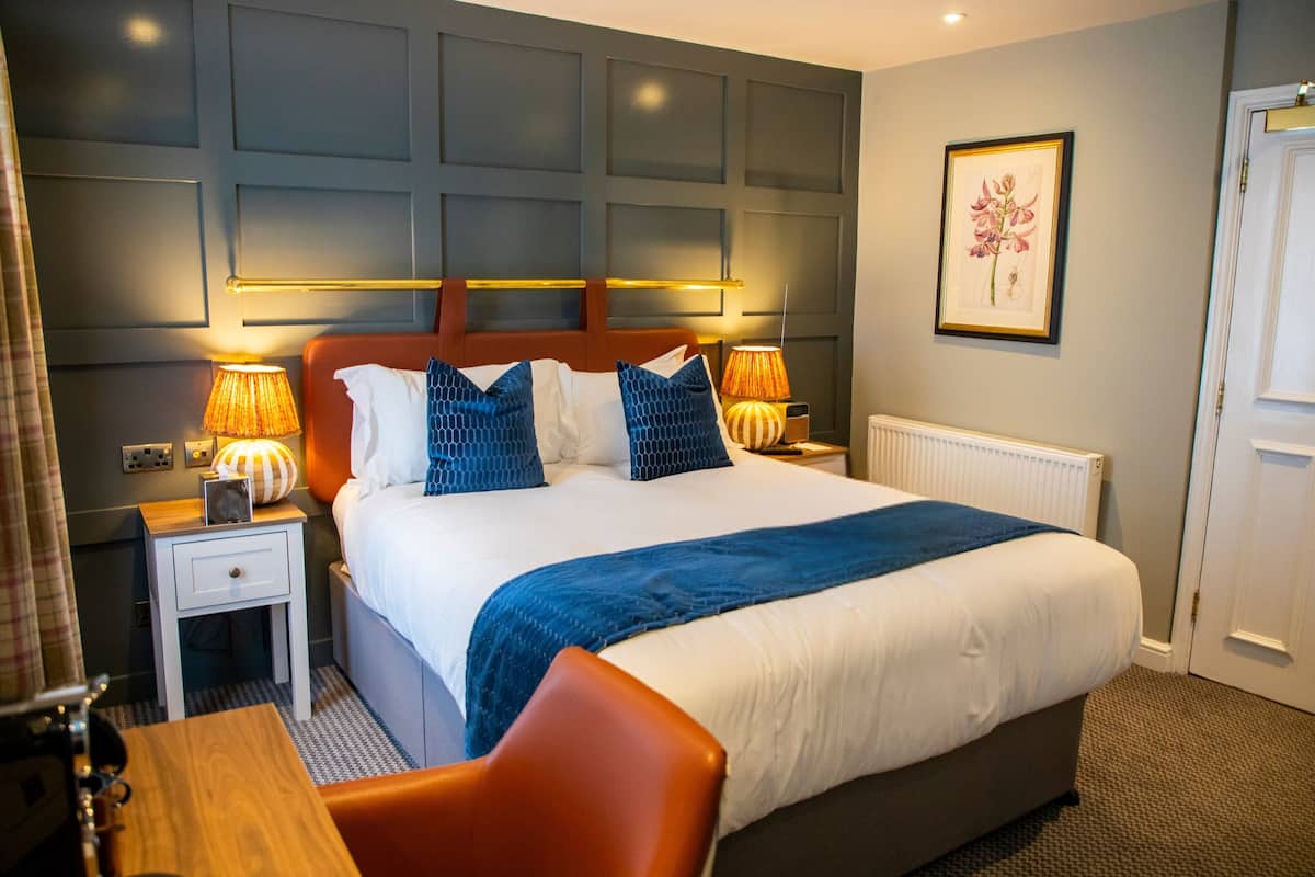 A hotel room with a large bed, bedside lamps, a framed picture on the wall, and a door to the right.