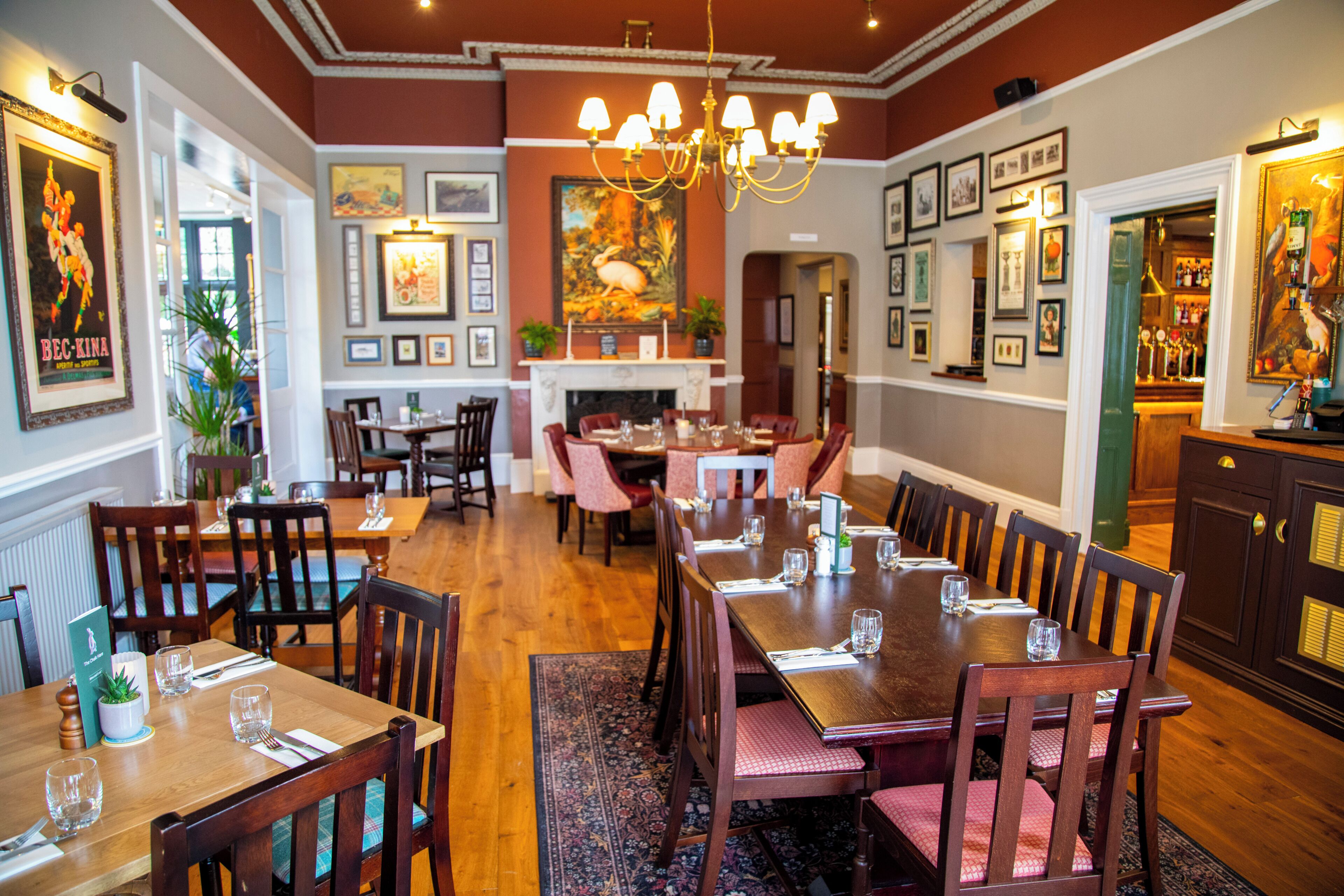 Un restaurante con mesas y sillas de madera, un candelabro, cuadros en las paredes y una chimenea.