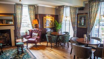 A cozy room with a fireplace, a round table with chairs, a red armchair, and patterned curtains.