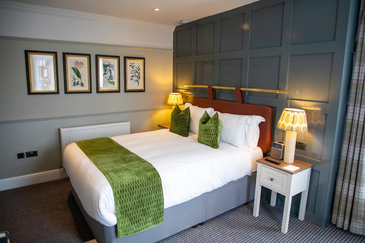 A hotel room with a bed, bedside lamps, a nightstand, and framed artwork on the wall.