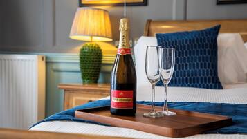A bottle of champagne and two glasses on a wooden tray on a bed with a blue blanket.