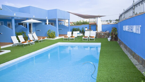 A pool area with blue walls, white lounge chairs, and a clear blue pool. - Be Cool Resort - Adults Only (San Bartolomé de Tirajana)