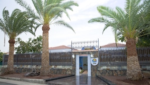 A gated entrance with palm trees, a stone wall, and a tiled roof. - Be Cool Resort - Adults Only (San Bartolomé de Tirajana)