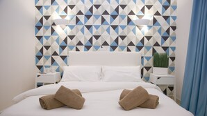 A neatly made bed with two towels, a geometric-patterned wall, and a small plant on a bedside table. - Be Cool Resort - Adults Only (San Bartolomé de Tirajana)
