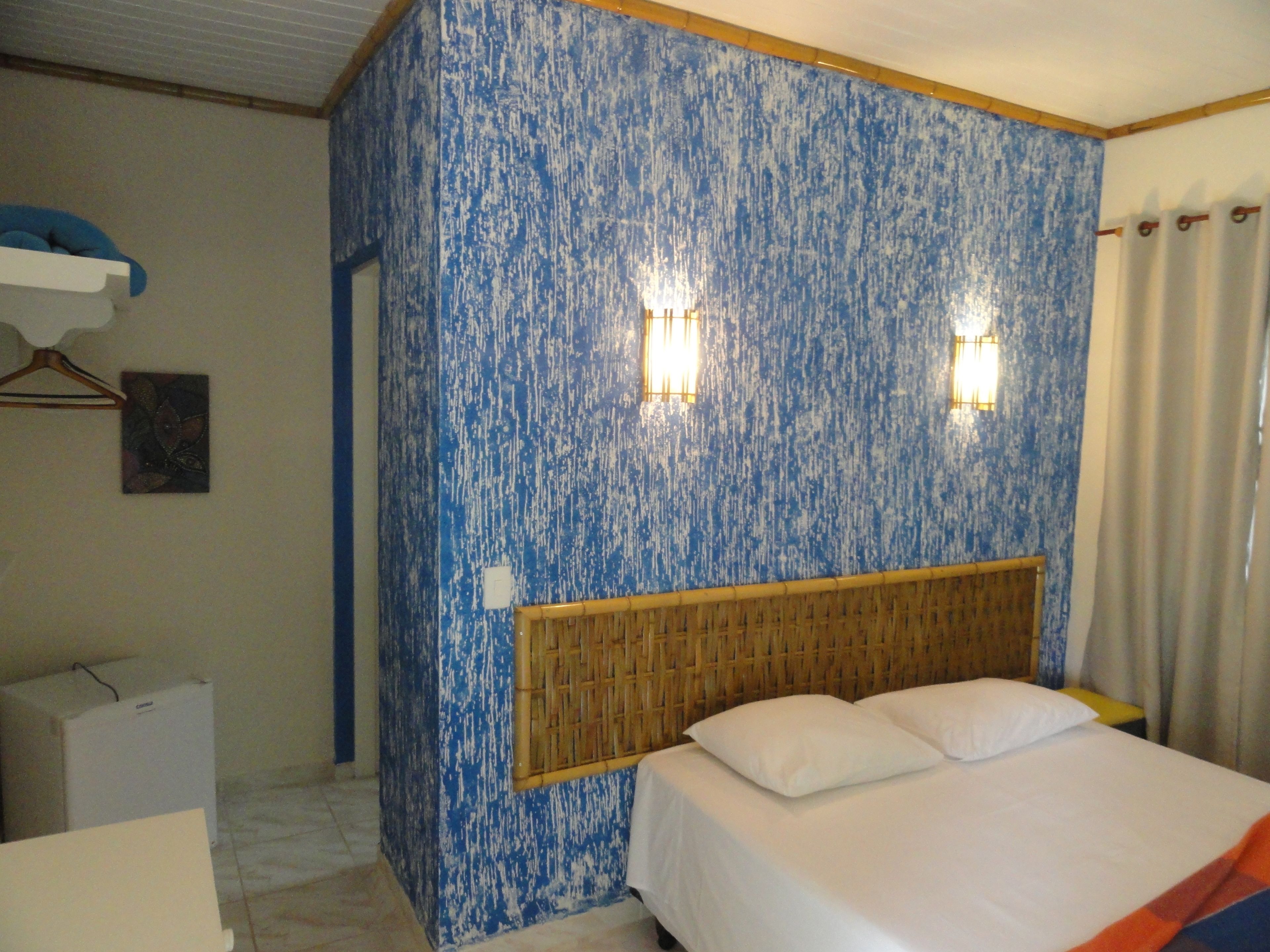 A hotel room with a bed, a wall with a blue textured pattern, two wall-mounted lights, and a wooden headboard.