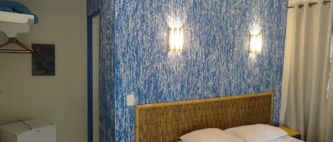 A hotel room with a bed, a wall with a blue textured pattern, two wall-mounted lights, and a wooden headboard.