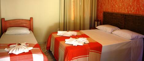 A hotel room with two single beds, each with a red and white checkered bedspread and a neatly folded white towel. The room has a wooden headboard and a red textured wall.