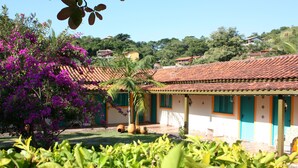 Uma casa tradicional com telhado de cerâmica, rodeada por vegetação exuberante e uma árvore florida.