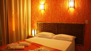 Quarto de hotel com cama, duas luminárias de cabeceira, painel de cabeceira trançado e colcha vermelha.