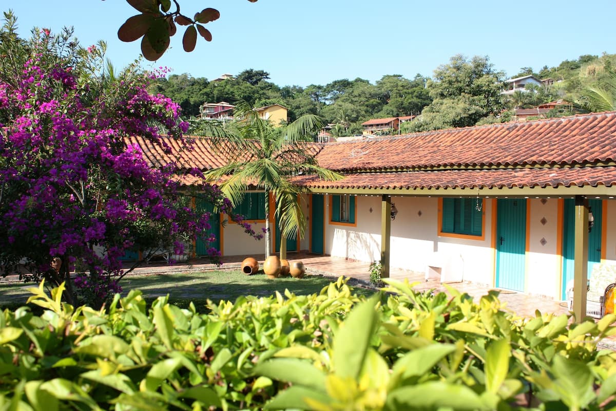 A house with a tiled roof, a garden with bougainvillea, and a view of a hill with other houses.