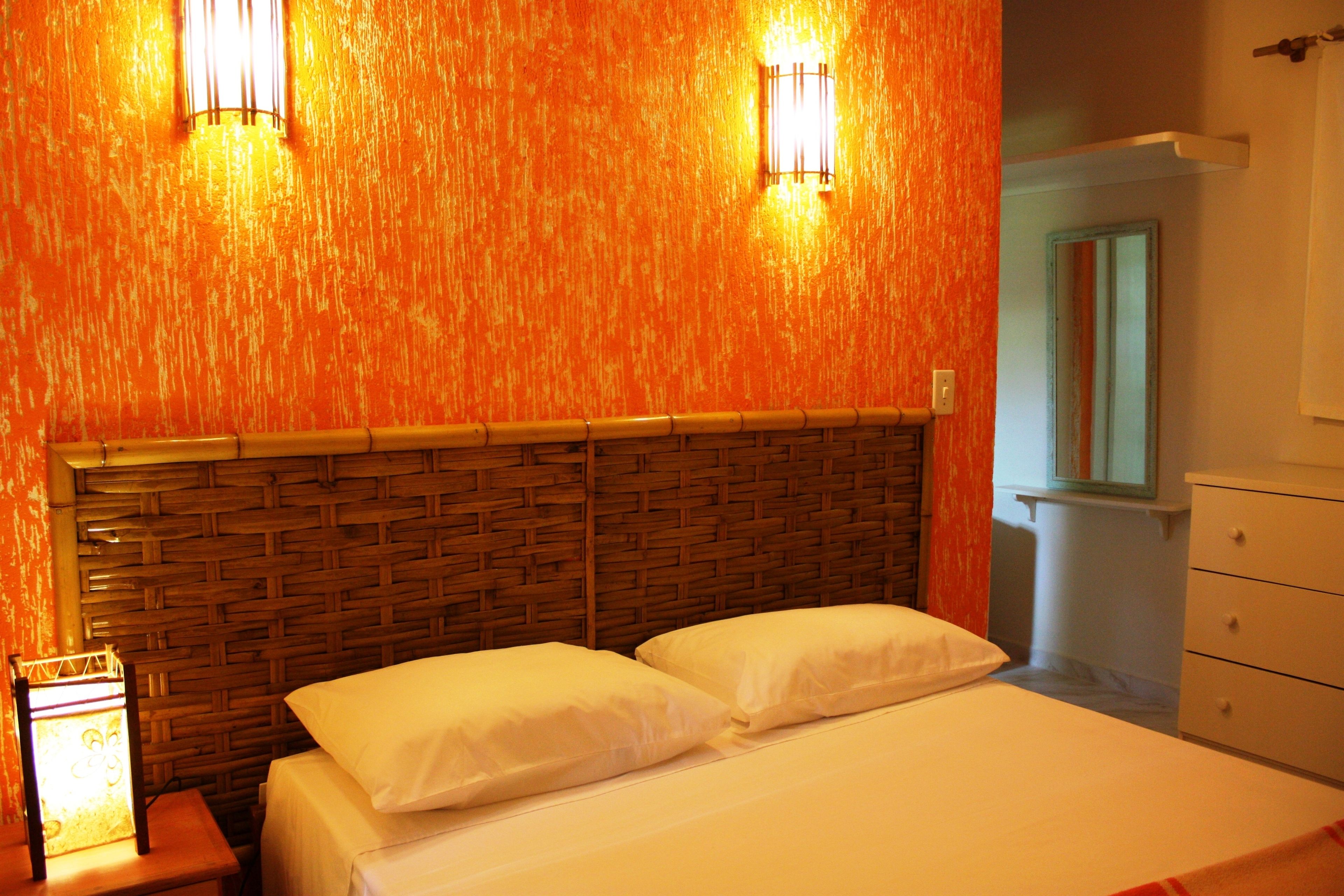 A room with a bed, two wall-mounted lights, a wooden headboard, and a nightstand with a lamp.