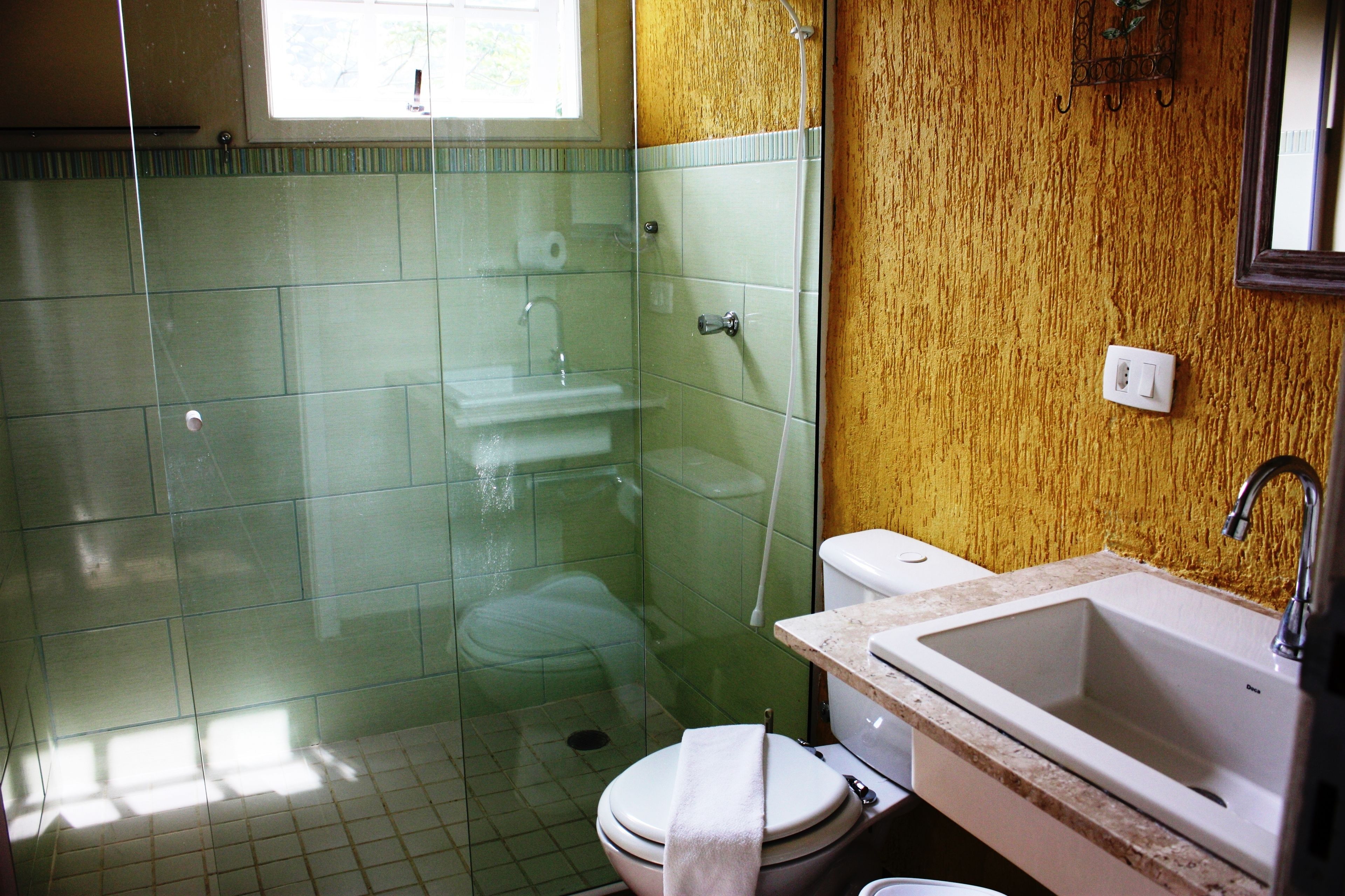 Et badeværelse med bruseniche, toilet og håndvask med spejl over.