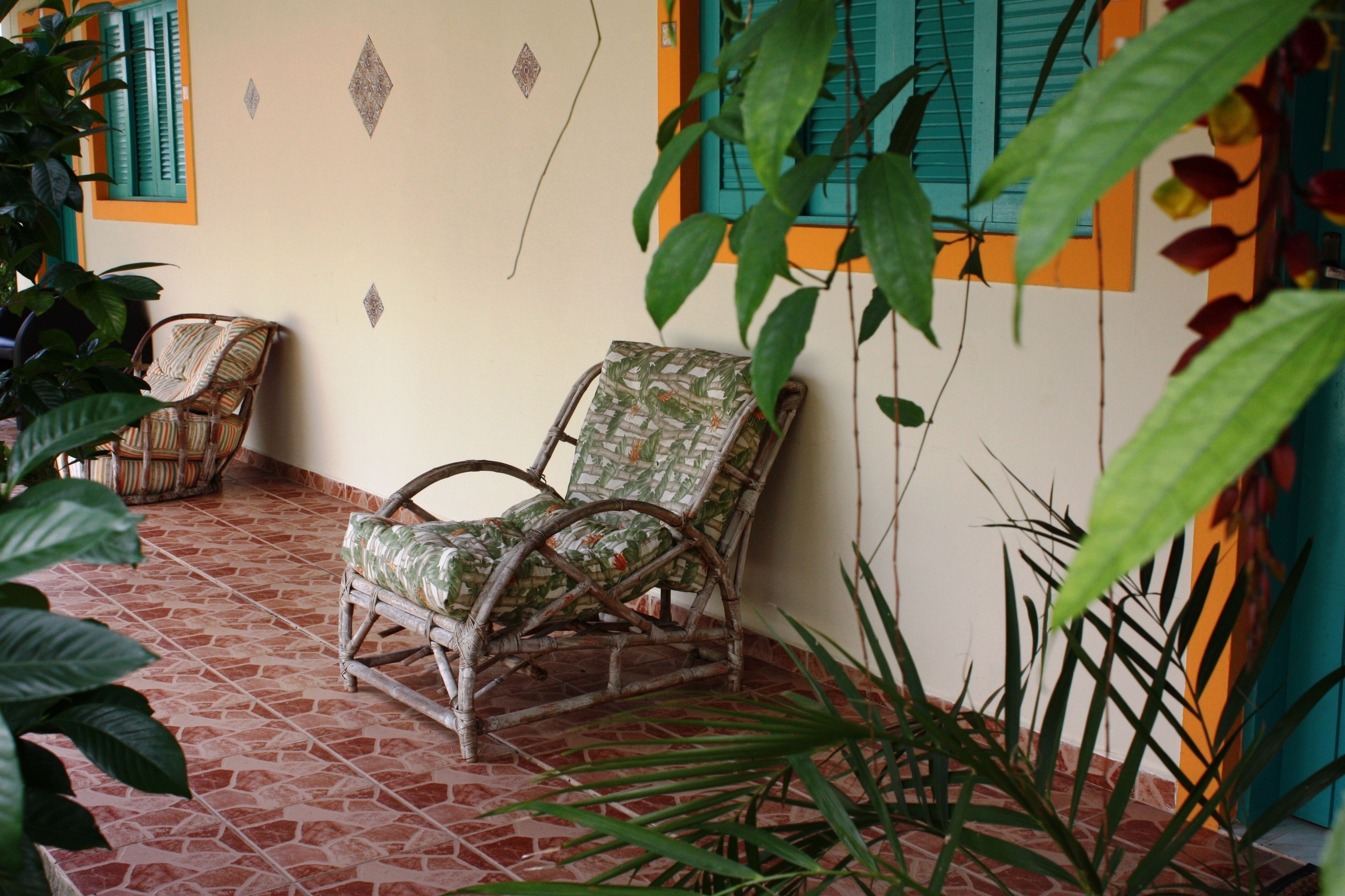 A wicker chair with a patterned cushion, a tiled floor, and a wall with decorative elements.