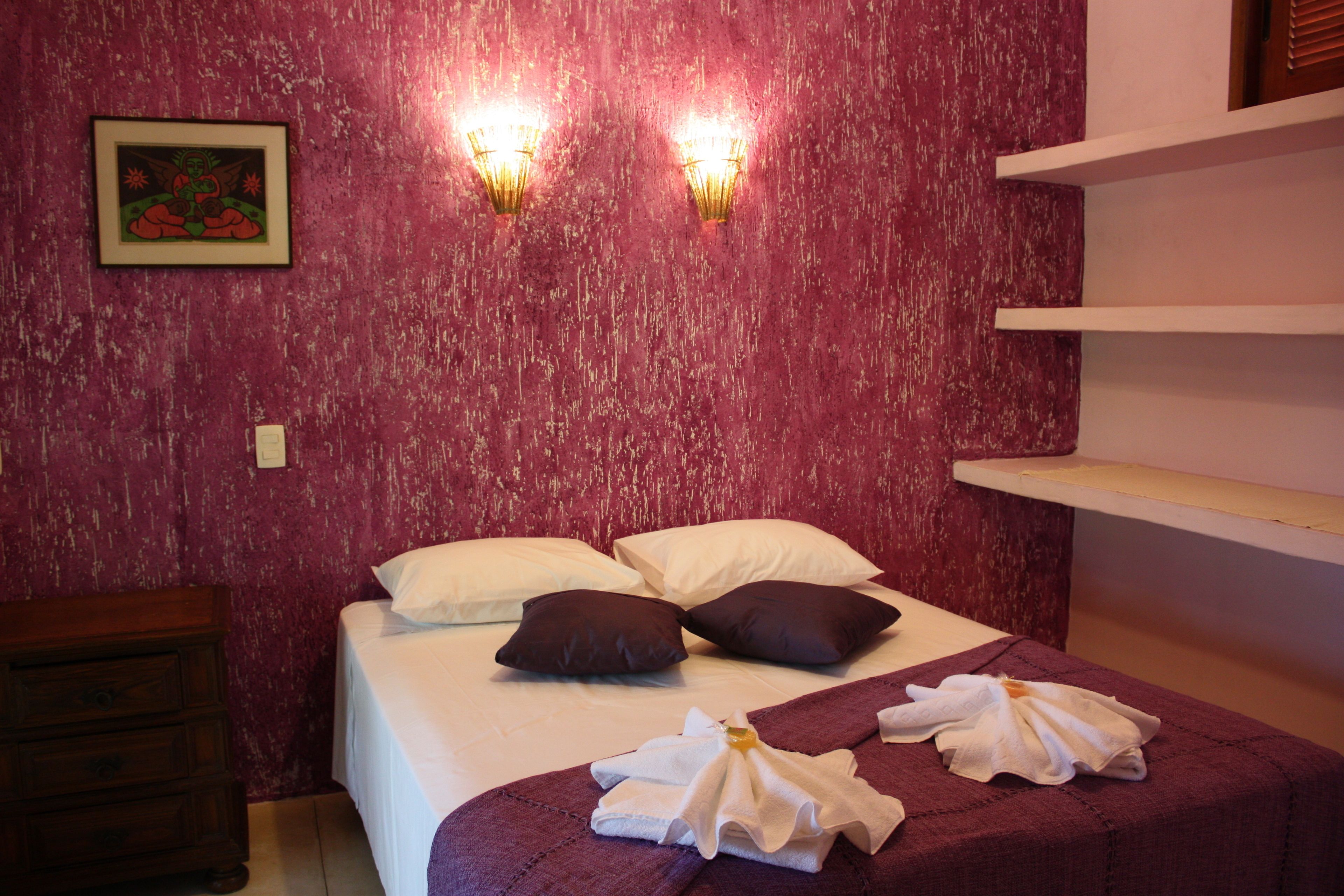 Quarto de hotel com cama, almofadas, mesa de cabeceira e um quadro na parede.