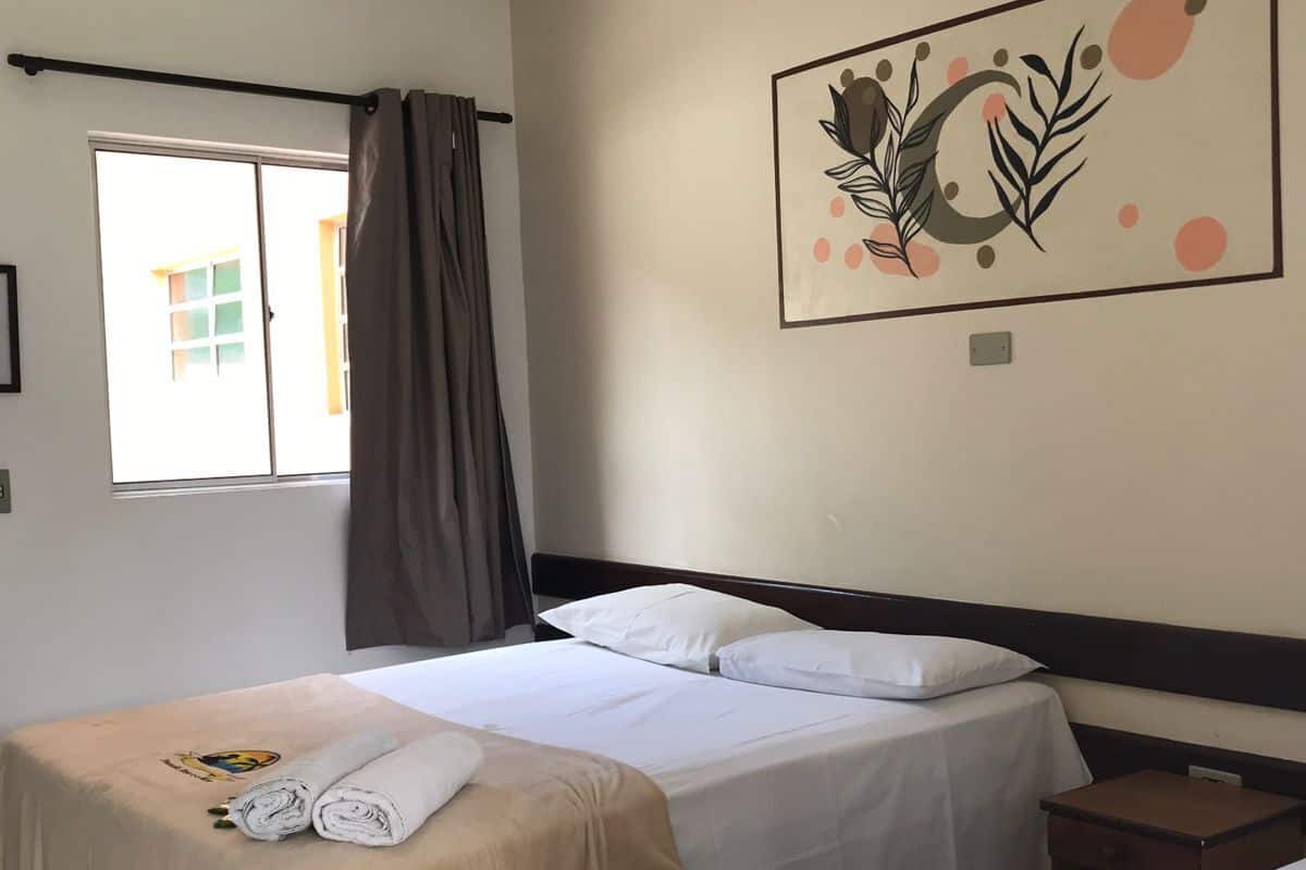 Ein Hotelzimmer mit zwei Betten, einem Deckenventilator, einem Fenster mit Vorhängen und einer Wand mit einem dekorativen Gemälde.