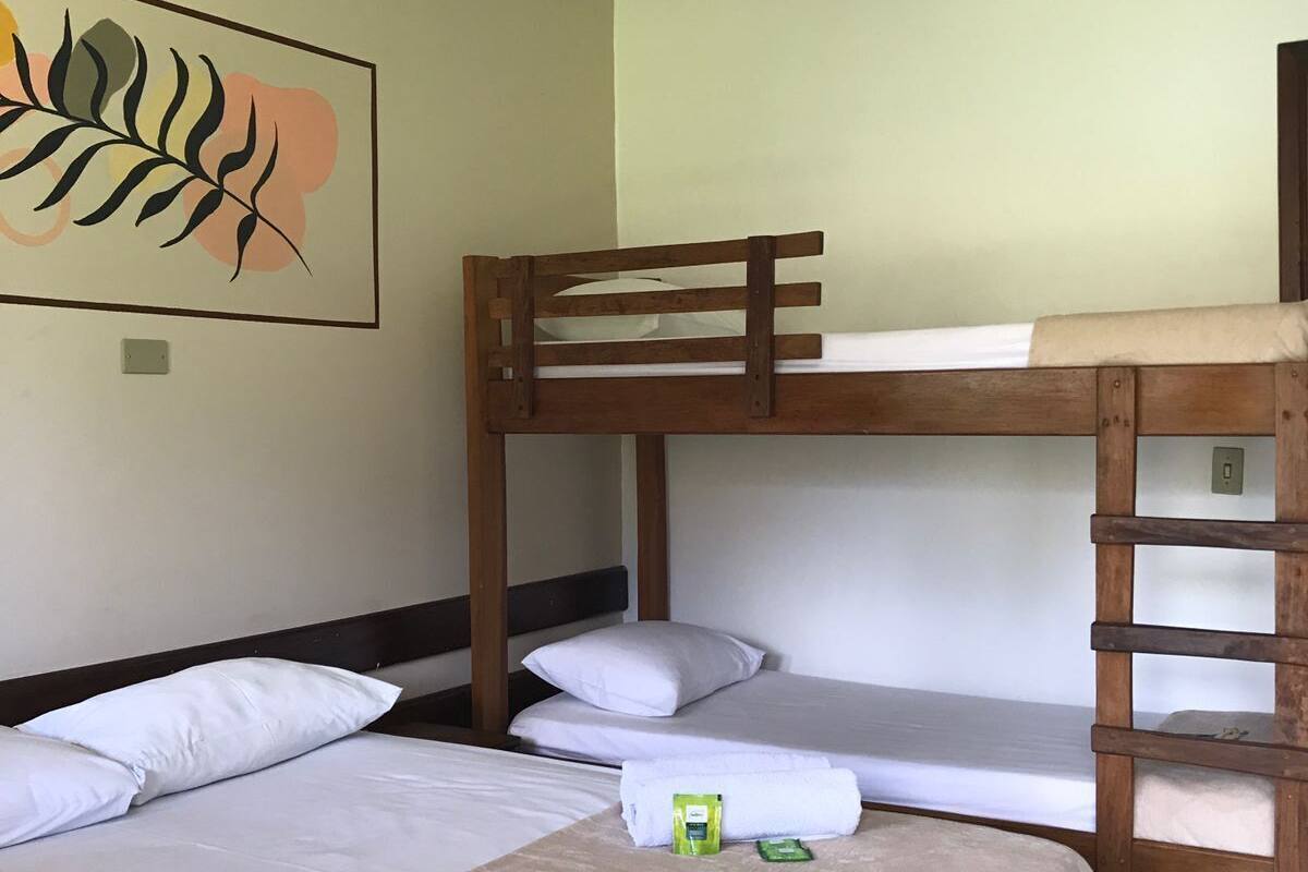 Ein Schlafraum mit Etagenbetten, einem Deckenventilator, einem Bett mit weißer Matratze und Kissen sowie einem gerahmten Kunstwerk an der Wand.